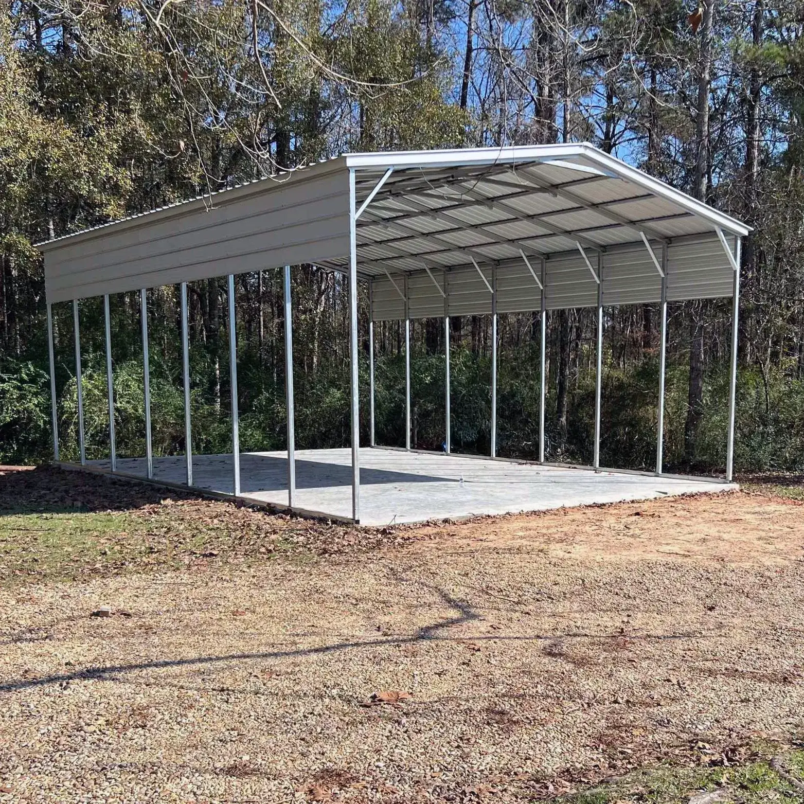 White metal rv carport nestled in a wooded area with lush green trees.
